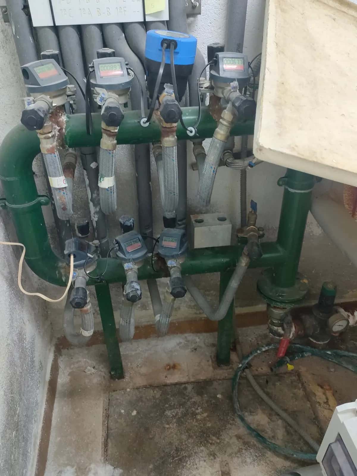 Batería de contadores de agua sobre un colector verde en un cuarto técnico