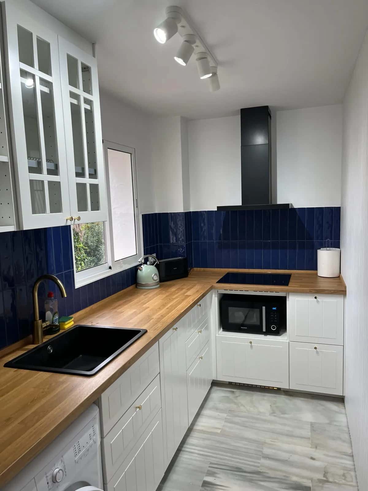 Cocina reformada con fregadero negro bajo encimera de madera y azulejo azul