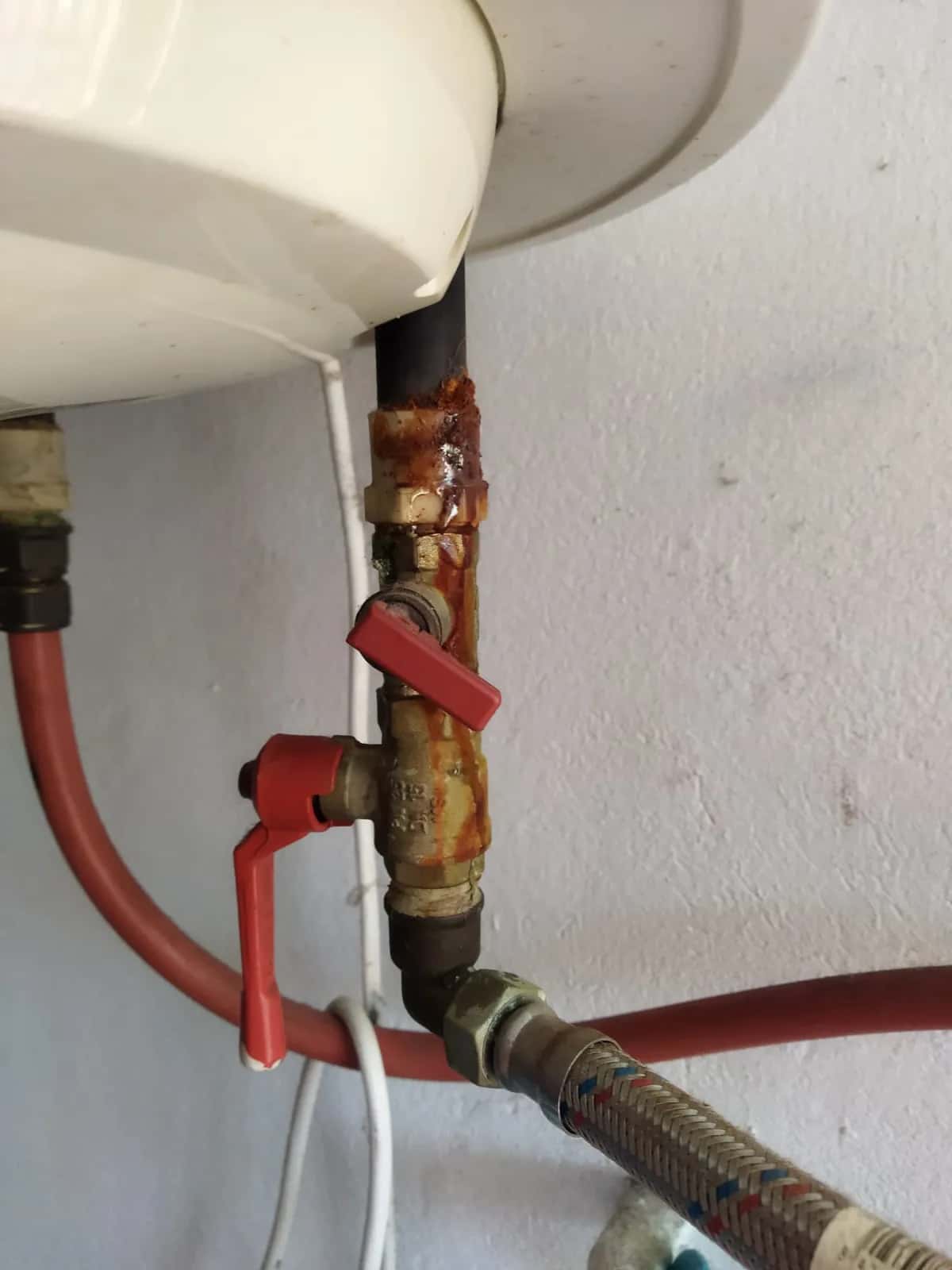 Conexión oxidada con llave de paso roja bajo un termo eléctrico