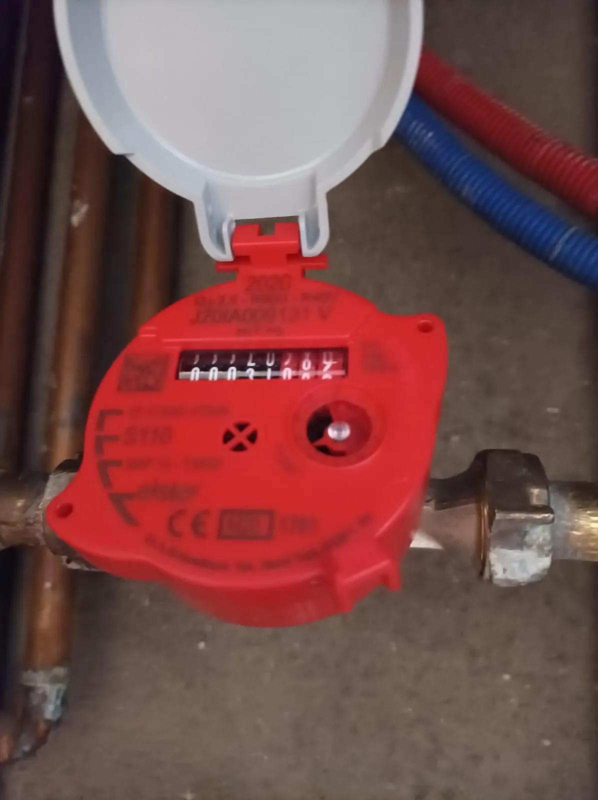 Contador de agua rojo con la tapa abierta instalado en tubería de cobre