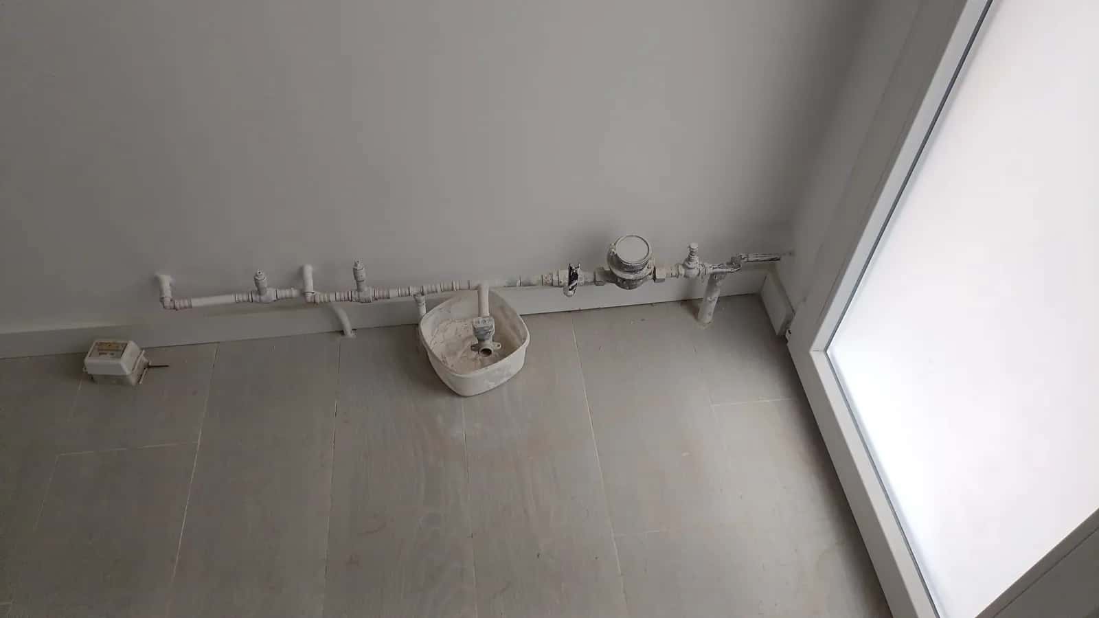 Contador de agua y tomas de fontanería junto al rodapié de una cocina vacía