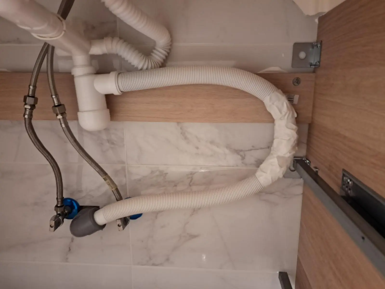 Desagüe y latiguillos de conexión bajo el fregadero dentro de un mueble de cocina