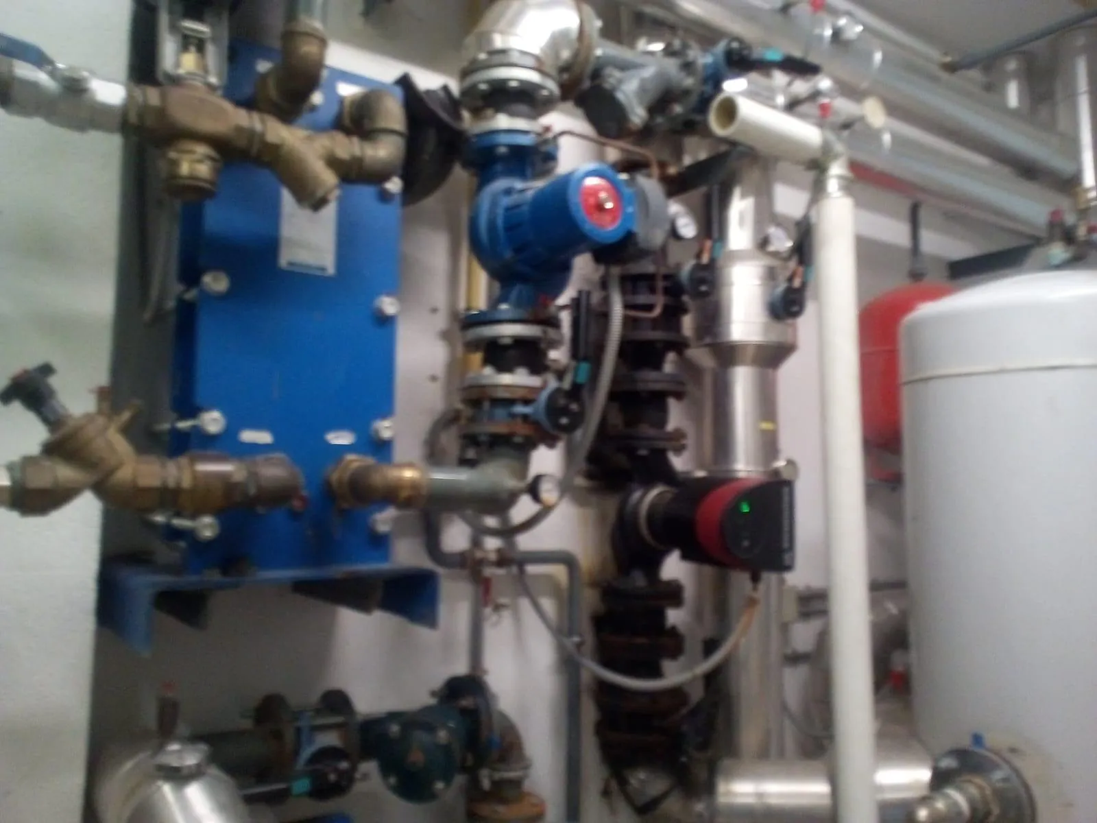 Intercambiador de placas azul con bombas y valvulería en una sala de calderas