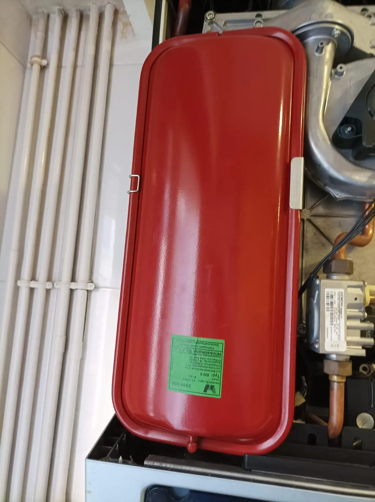 Interior de una caldera abierta con vaso de expansión rojo y componentes internos