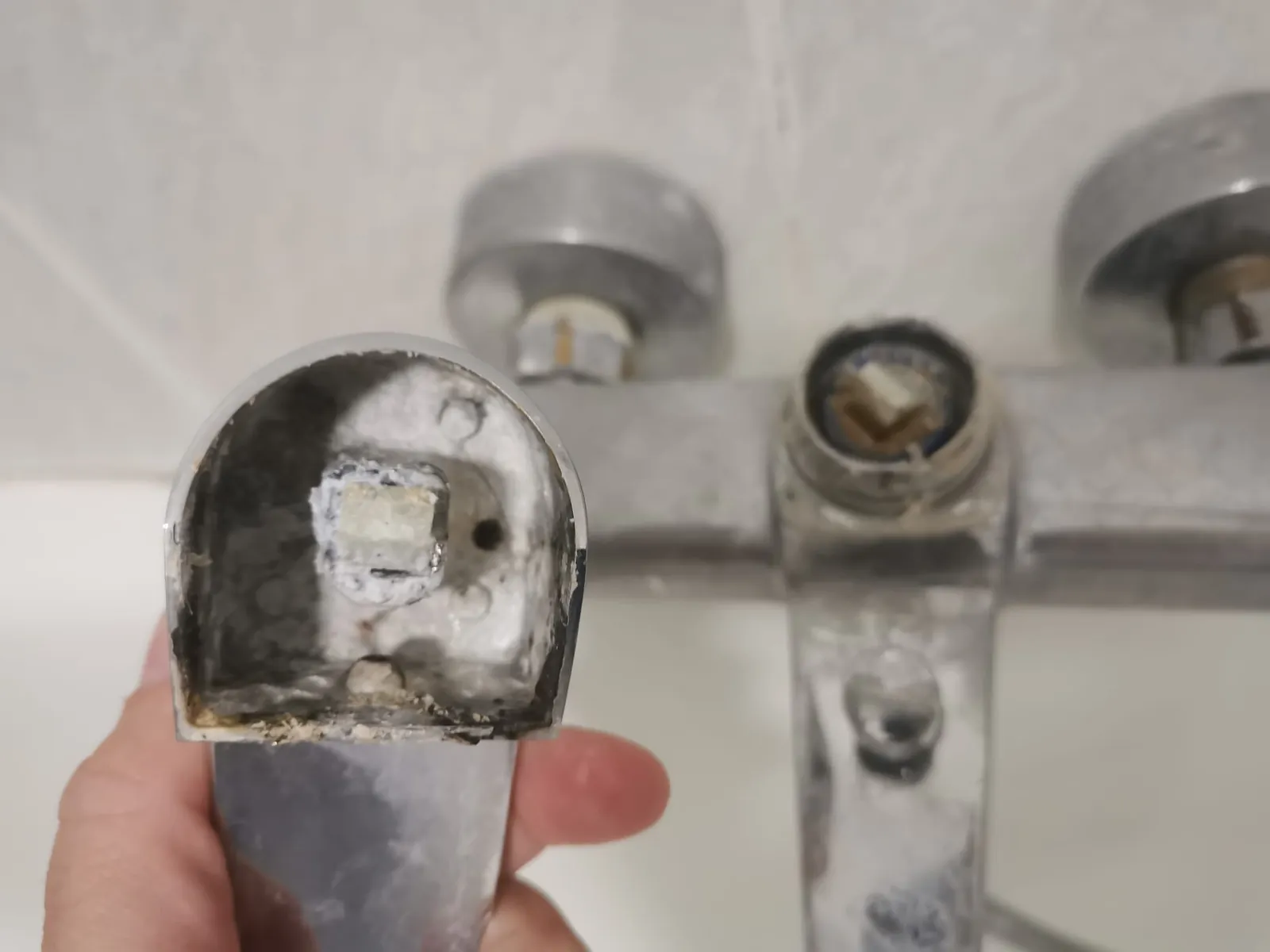 Mano sosteniendo la maneta rota de un grifo mezclador de bañera