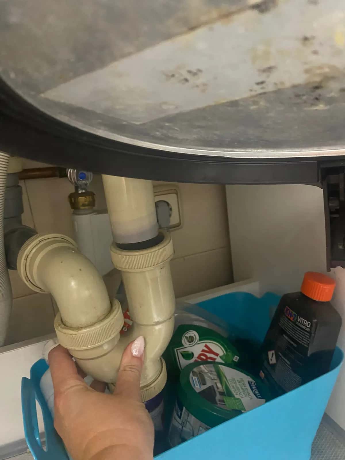 Mano revisando el sifón y el desagüe bajo el fregadero de una cocina