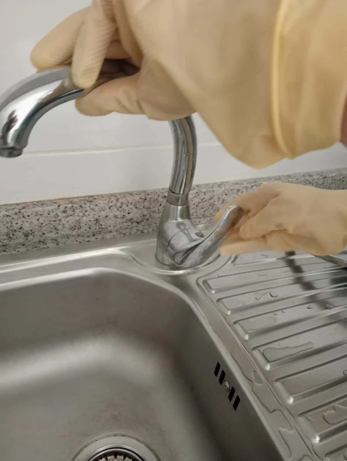 Manos con guantes revisando un grifo monomando de fregadero de acero