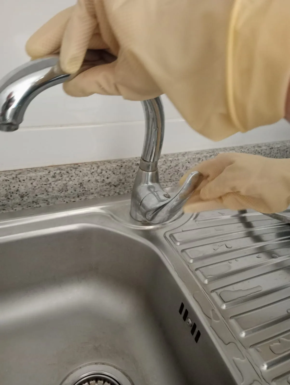 Manos con guantes revisando un grifo monomando de fregadero de acero