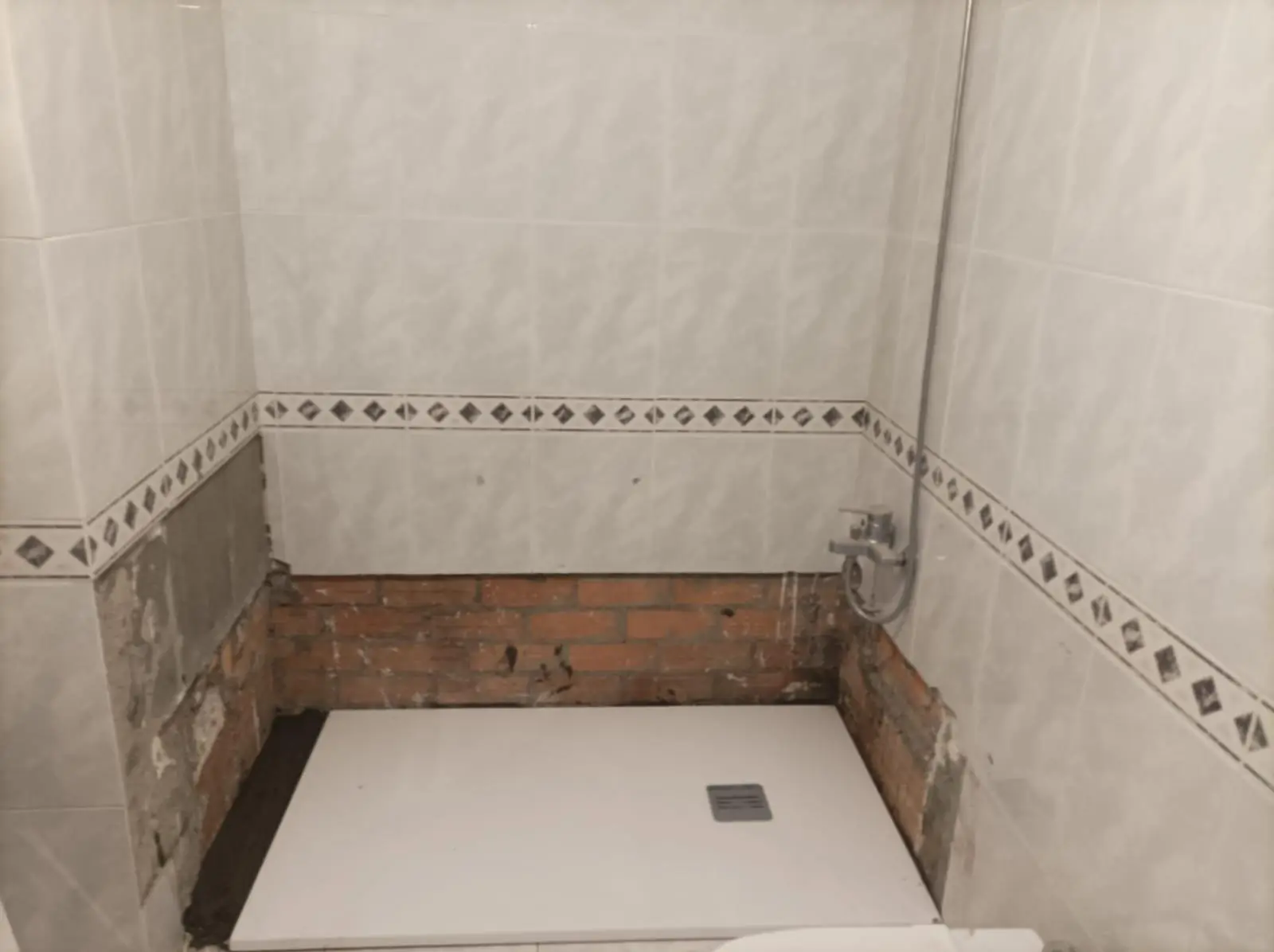 Plato de ducha nuevo colocado con parte del azulejo inferior retirado y ladrillo visto