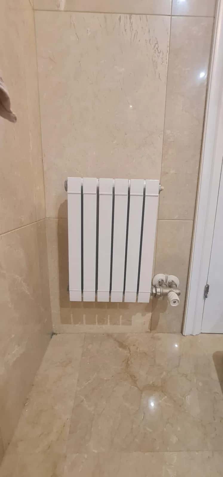 Radiador de aluminio blanco instalado en la pared de un baño de mármol