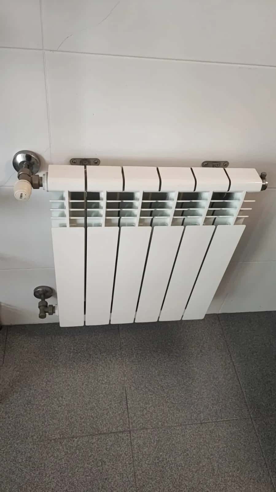 Radiador de aluminio blanco con llaves cromadas instalado en la pared de una cocina