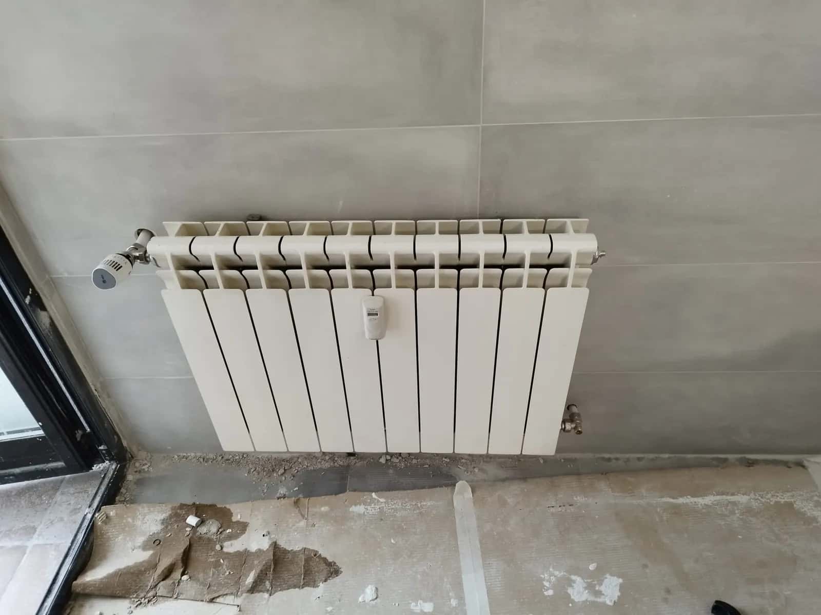 Radiador de aluminio con válvula termostática recién instalado en una vivienda en obra