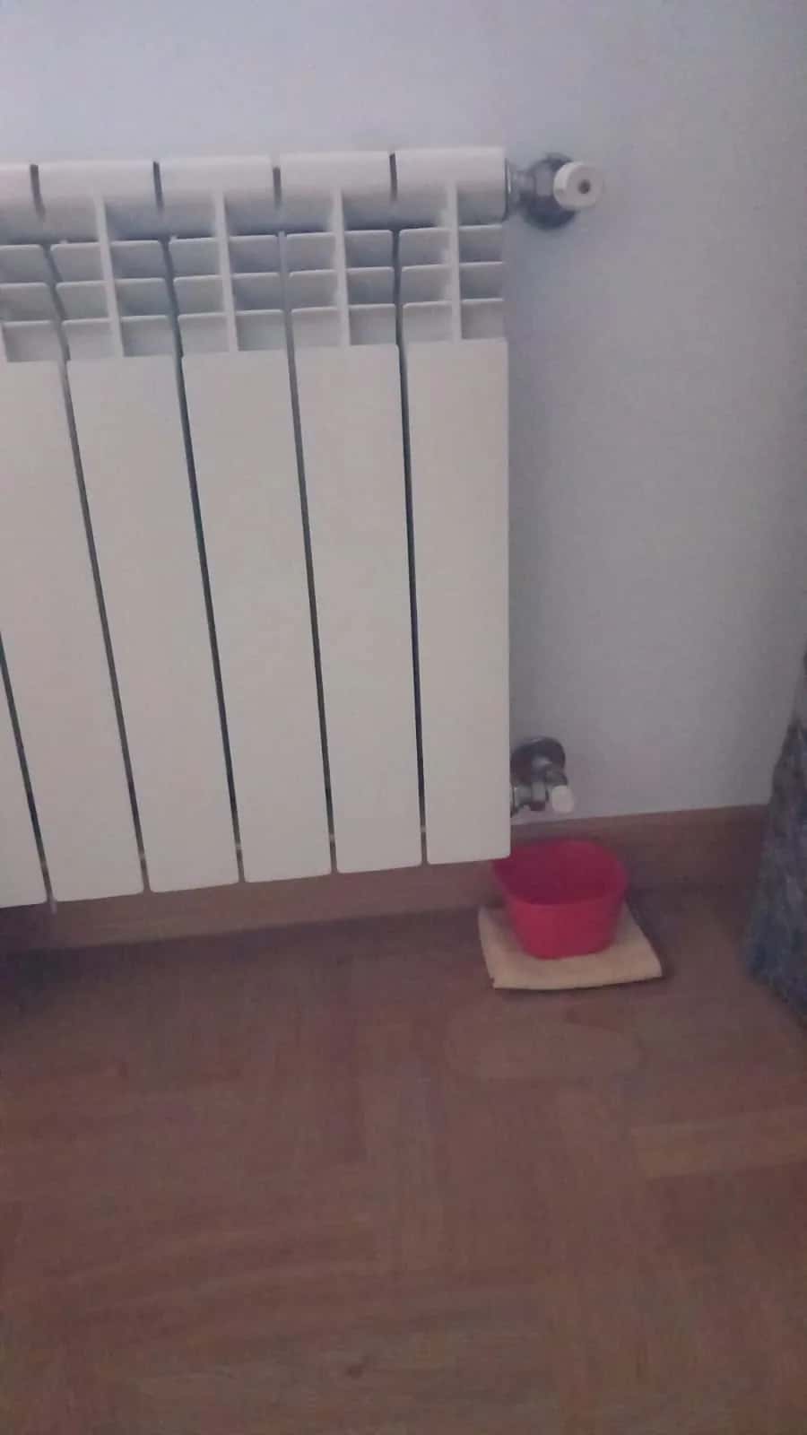 Radiador con un cubo rojo debajo para recoger el agua que gotea de la llave