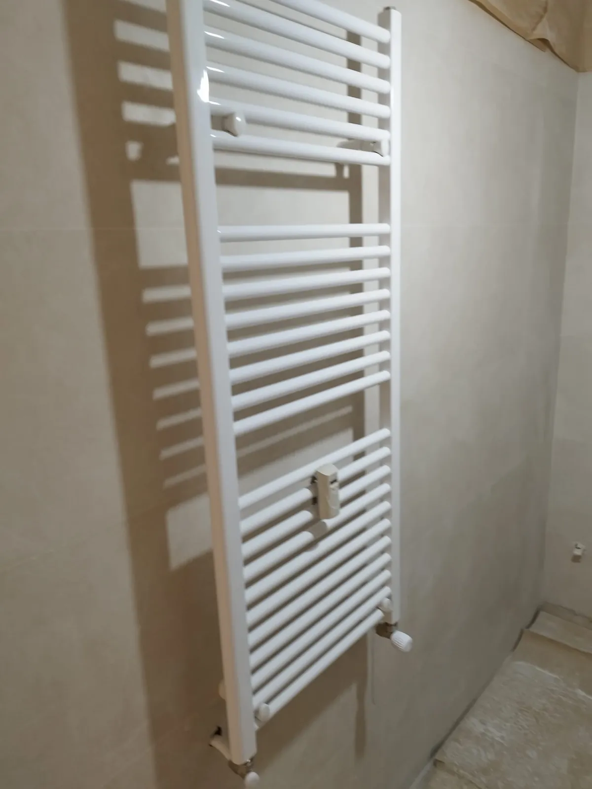 Radiador toallero blanco instalado en la pared de un baño en reforma