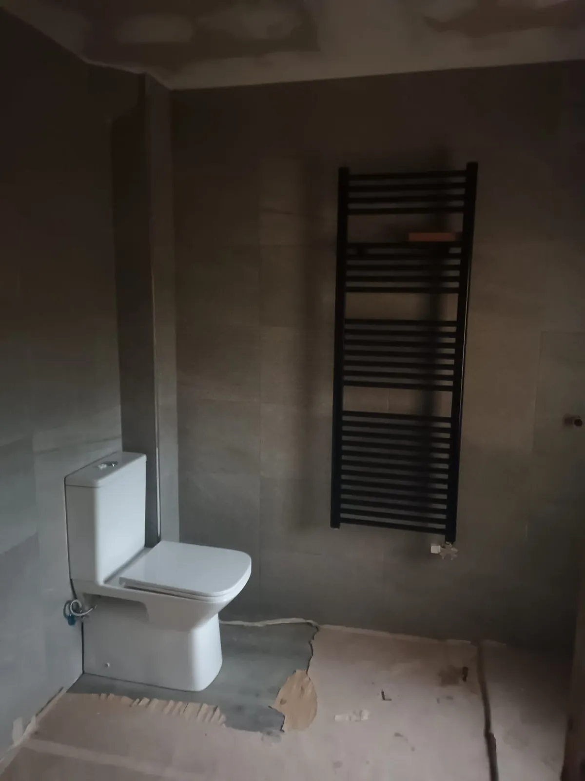 Radiador toallero negro e inodoro compacto en un baño de azulejo gris