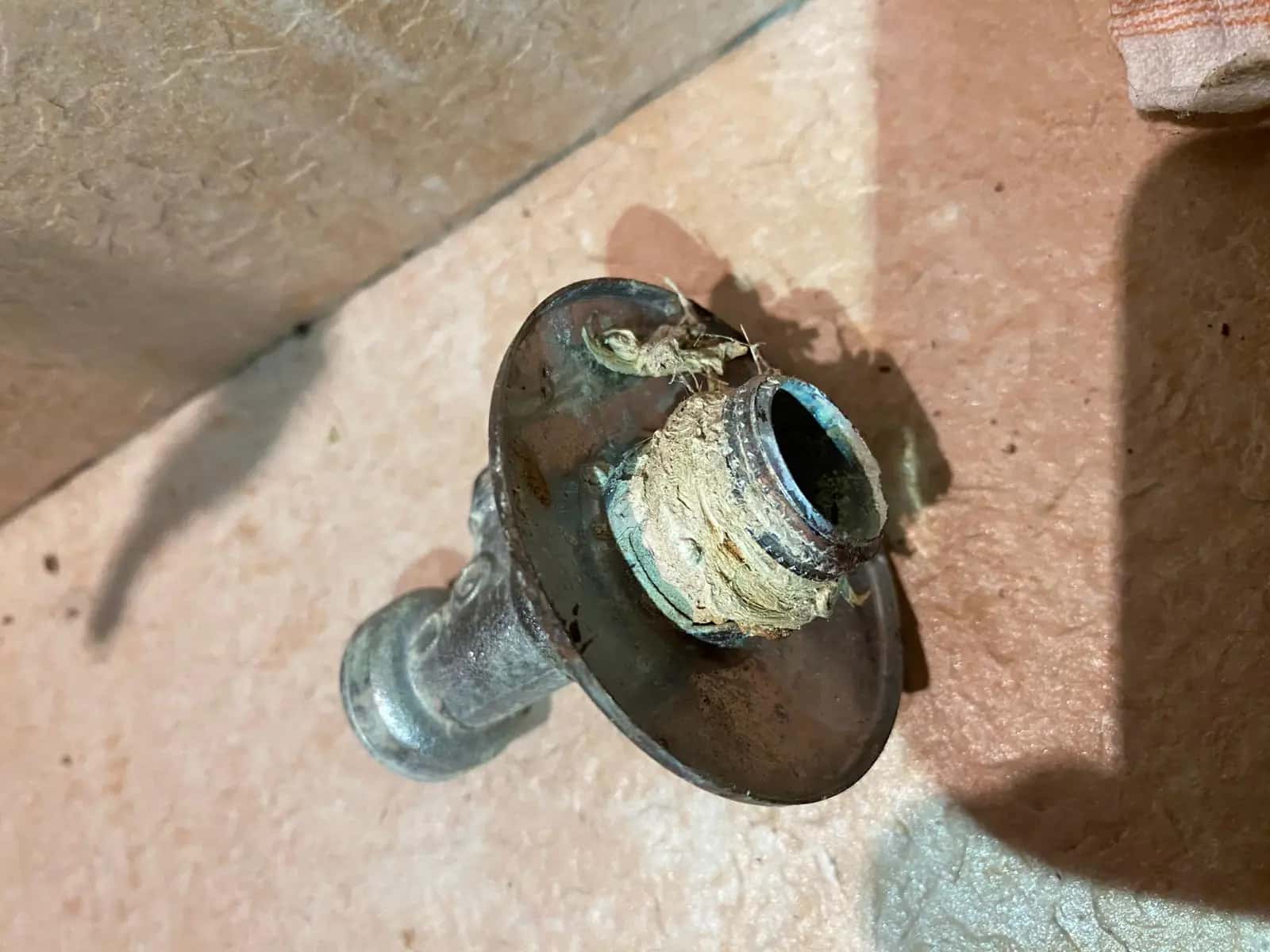 Salida de tubería corroída con restos de cáñamo en la rosca sobre suelo de obra