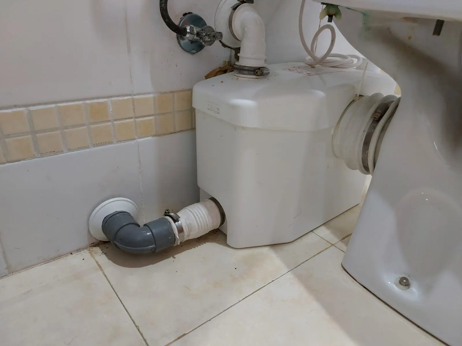 Triturador sanitario conectado a un inodoro con codo de desagüe gris en un baño