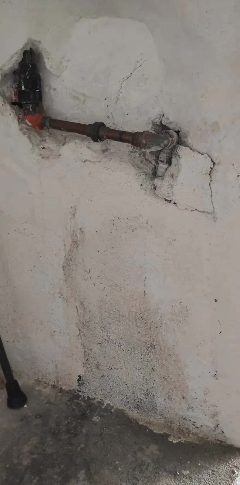Tubería de cobre en una pared picada con manchas de humedad debajo