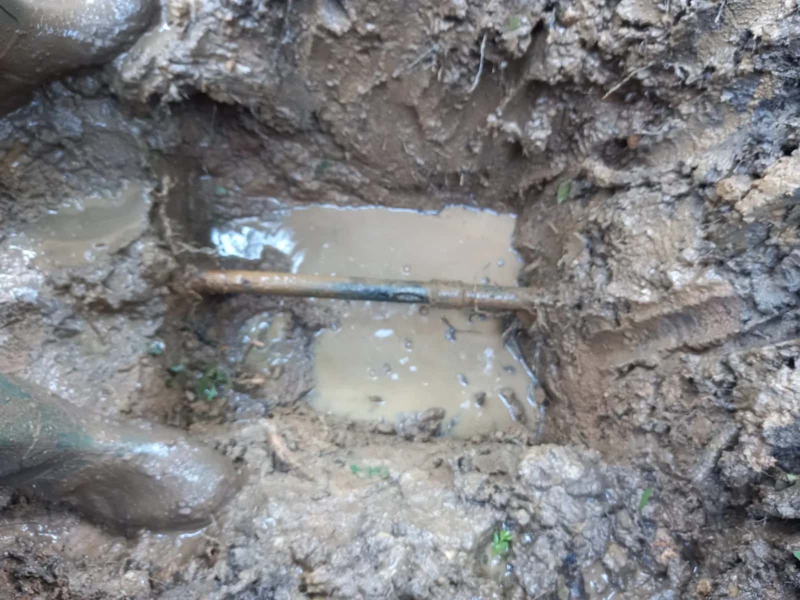 Tubería enterrada al descubierto en una excavación encharcada por una fuga