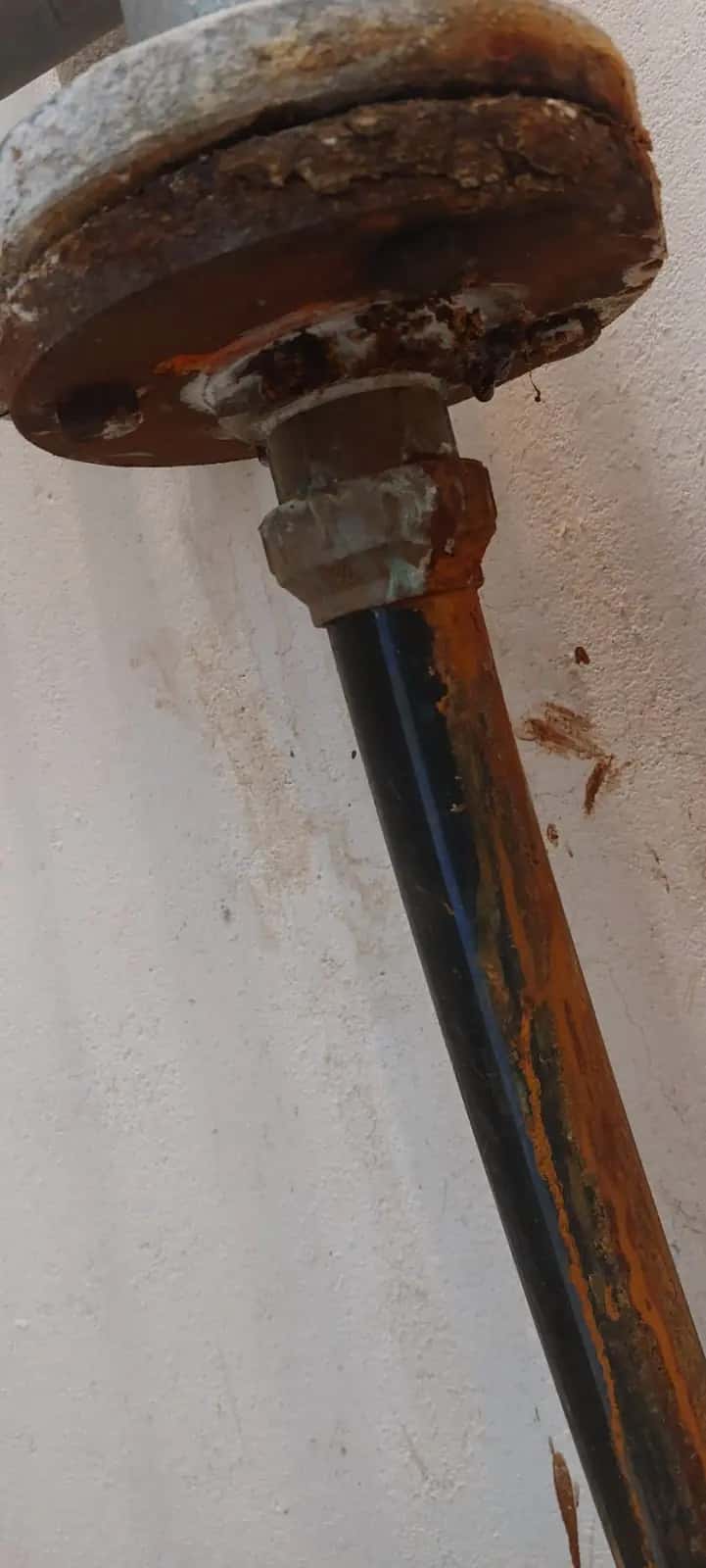 Tubería de hierro antigua con brida oxidada y restos de corrosión junto a una pared