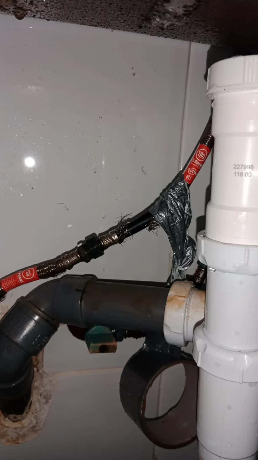 Tuberías de desagüe de PVC y latiguillos de agua bajo un lavabo