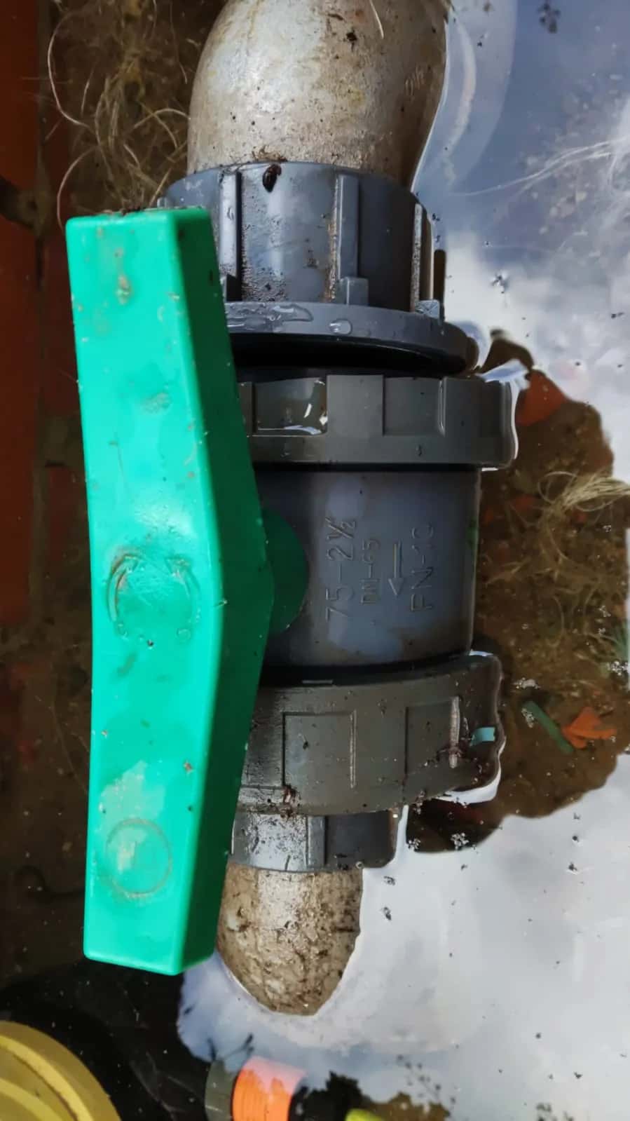 Válvula de bola de PVC con maneta verde en una tubería enterrada con agua