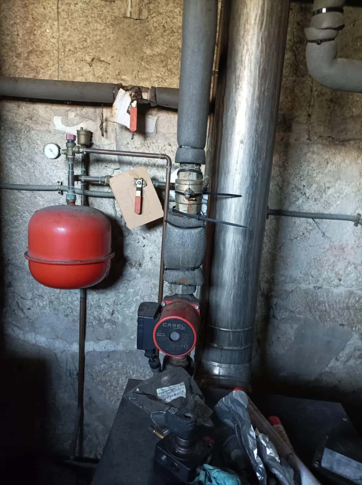 Vaso de expansión rojo, bomba circuladora y llaves de corte junto a una caldera de gasóleo